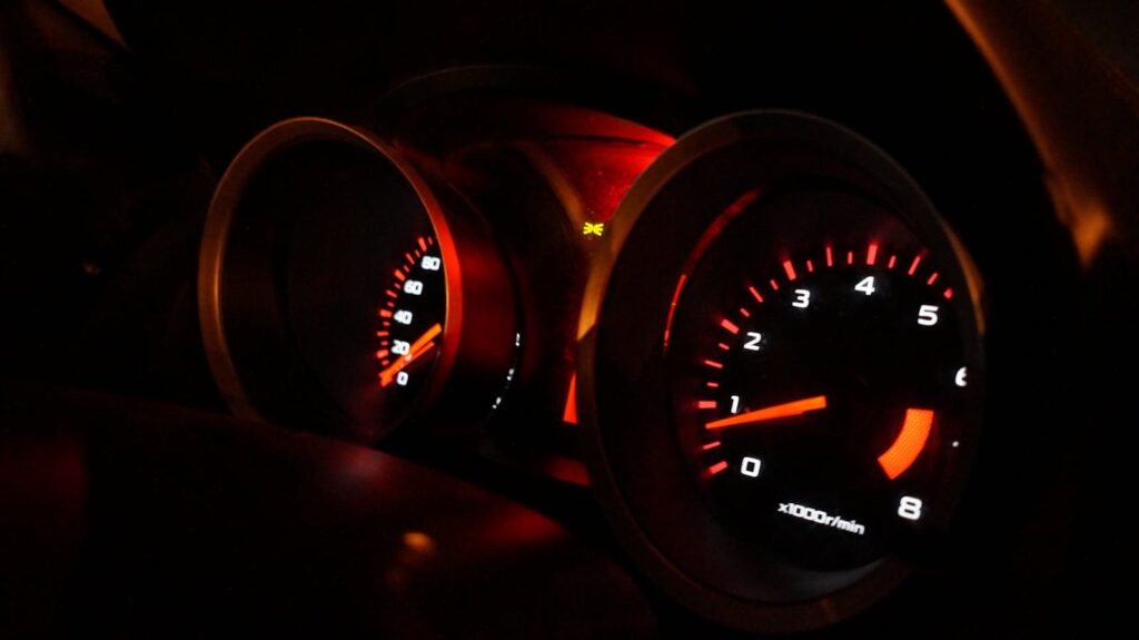 A detailed view of illuminated car gauges on the dashboard at night.